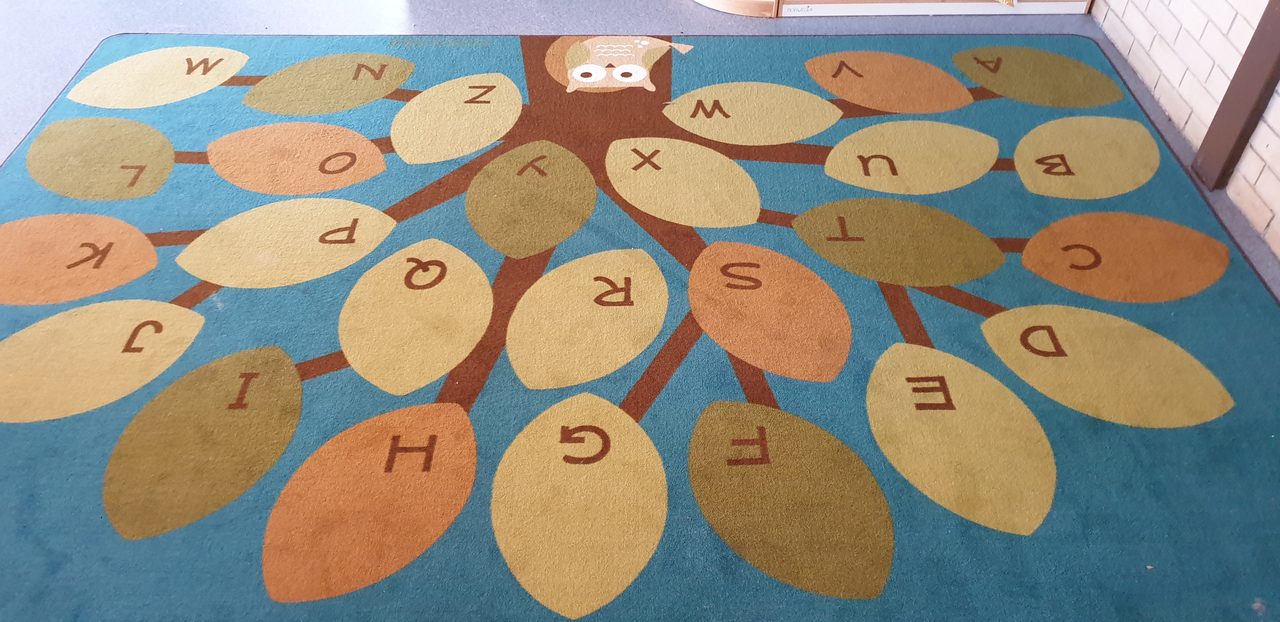 A teal alphabet rug in a Perth childcare room, cleaned first to take out the soil, because sanitising only works on a clean surface.