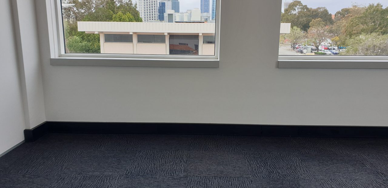 Charcoal carpet tiles under a Perth office window, little-walked tiles that can be swapped with the traffic route to even out the wear.