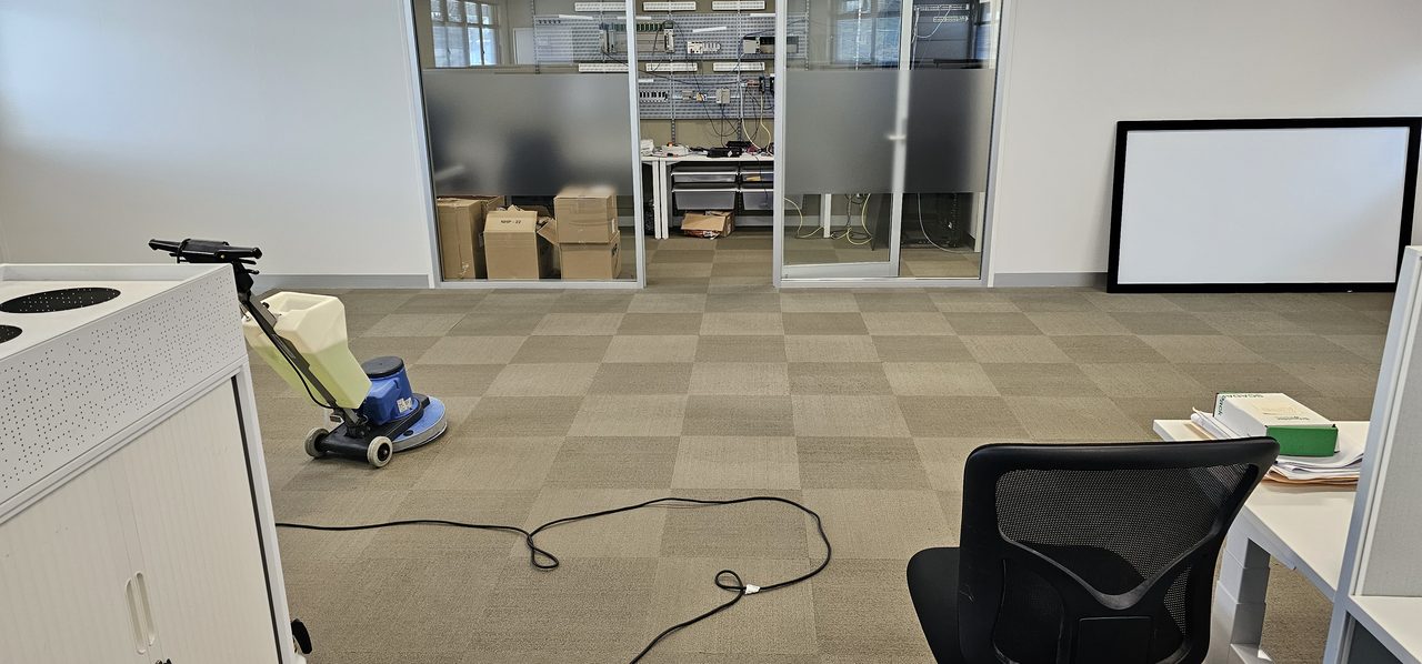 Machine scrubbing beige checkerboard carpet tiles in a Perth office, loosening soil that surface cleaning only pushes around
