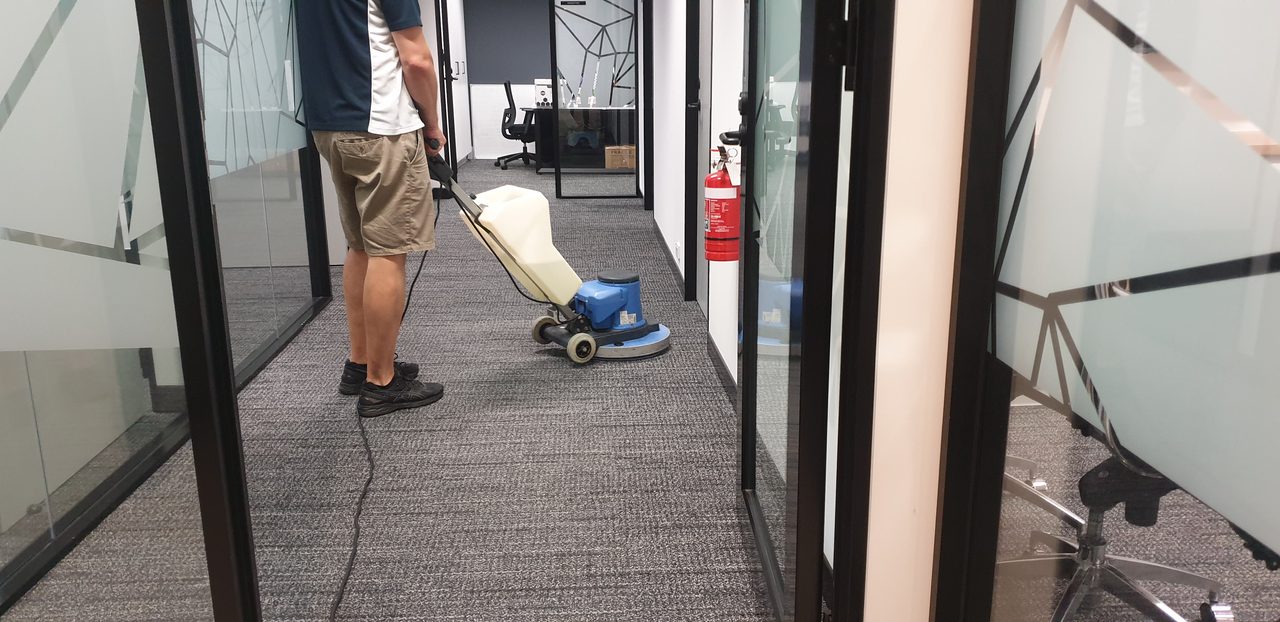 A glass walled corridor in a Perth office, its grey carpet tiles scrubbed clean along the full run between the meeting rooms