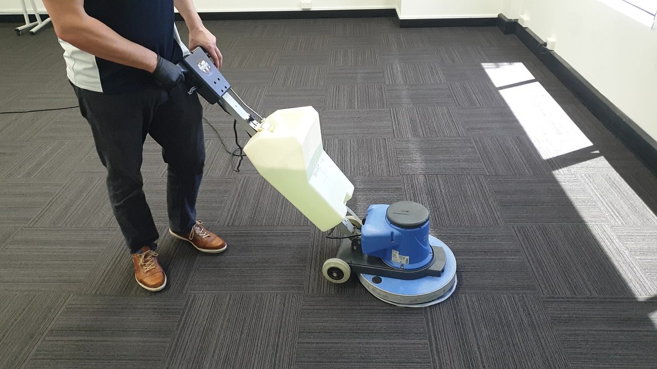A make good clean in progress on charcoal striped carpet tiles, the scrubbing machine covering a bright Perth office