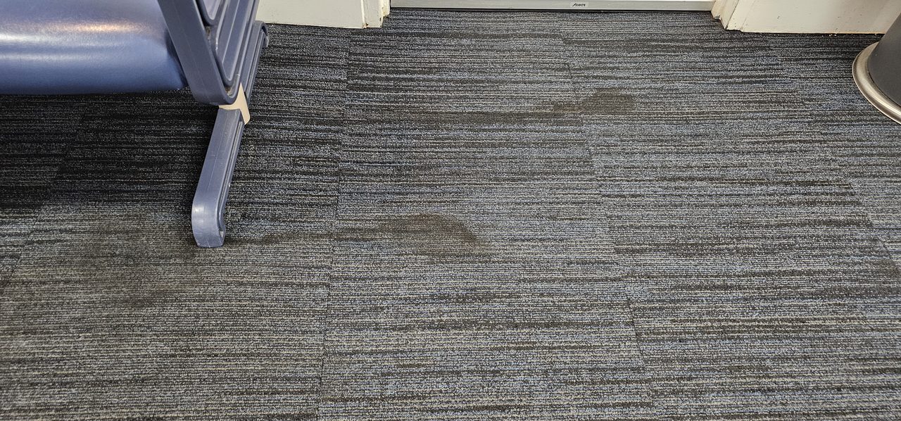 Greasy brown spill stains in the carpet tiles of a Perth waiting area, staining soil that bonds to the fibre and needs a spotter to shift