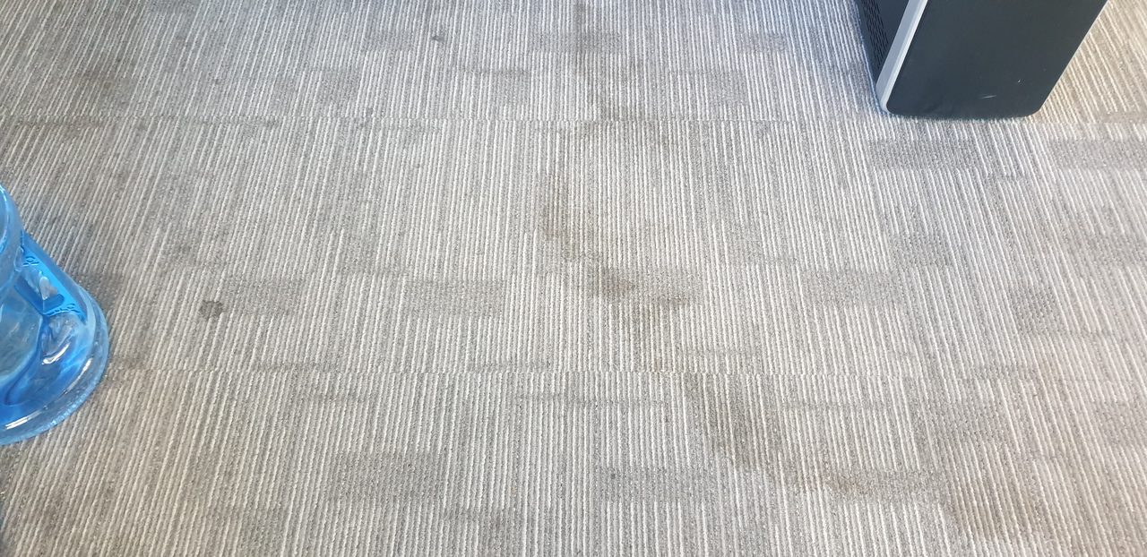 Blotchy traffic soil across pale grey carpet tiles in a Perth office, the high use zone that needs cleaning more often than the rest