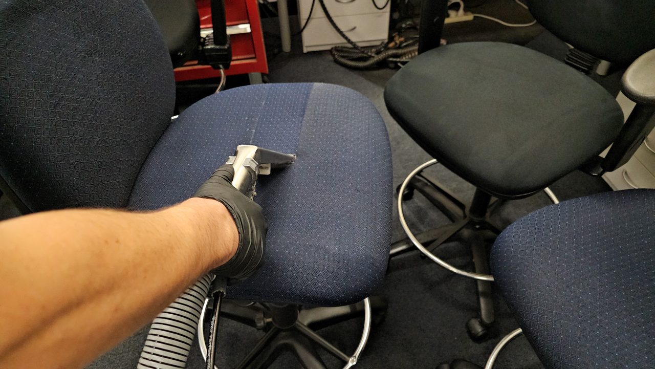 An upholstery tool drawing soil out of a navy fabric office chair in Perth, the cleaned band showing how much the seat was holding