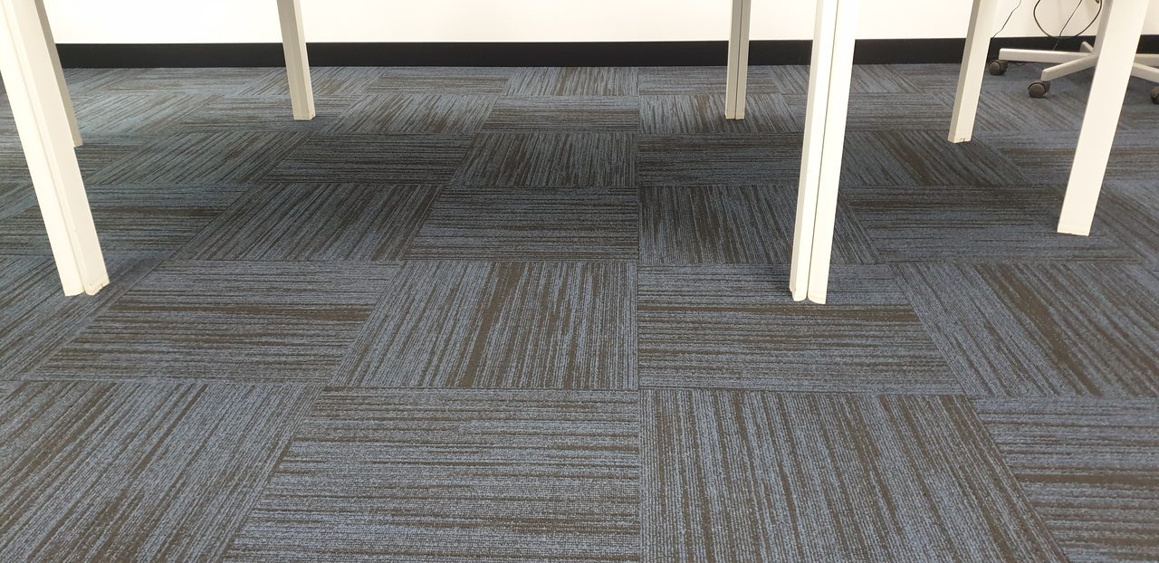 Blue grey linear carpet tiles beneath the tables of a Perth training room, cleaned clear of the soil that chairs and feet grind in