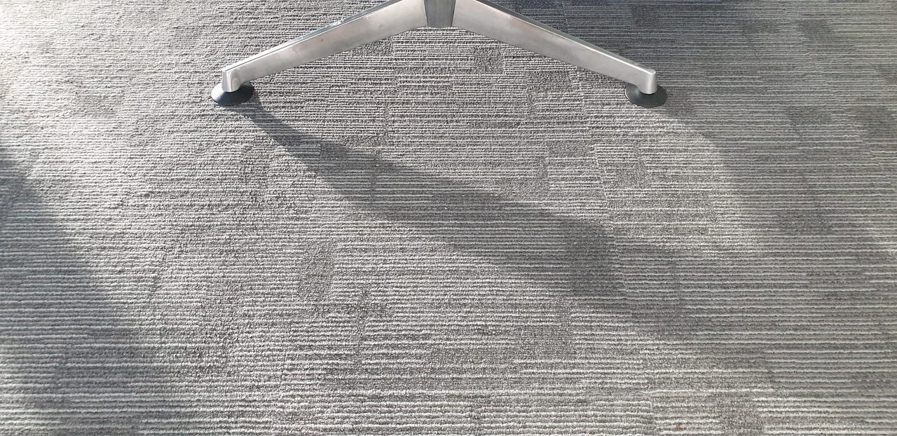 A grey soil shadow spread around an office chair base in Perth, the buildup a shared desk gathers from many users every day