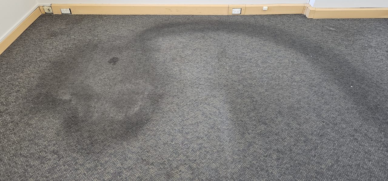 A large soil shadow on charcoal tweed loop carpet in a Perth office, the kind of buildup that smells musty after rain