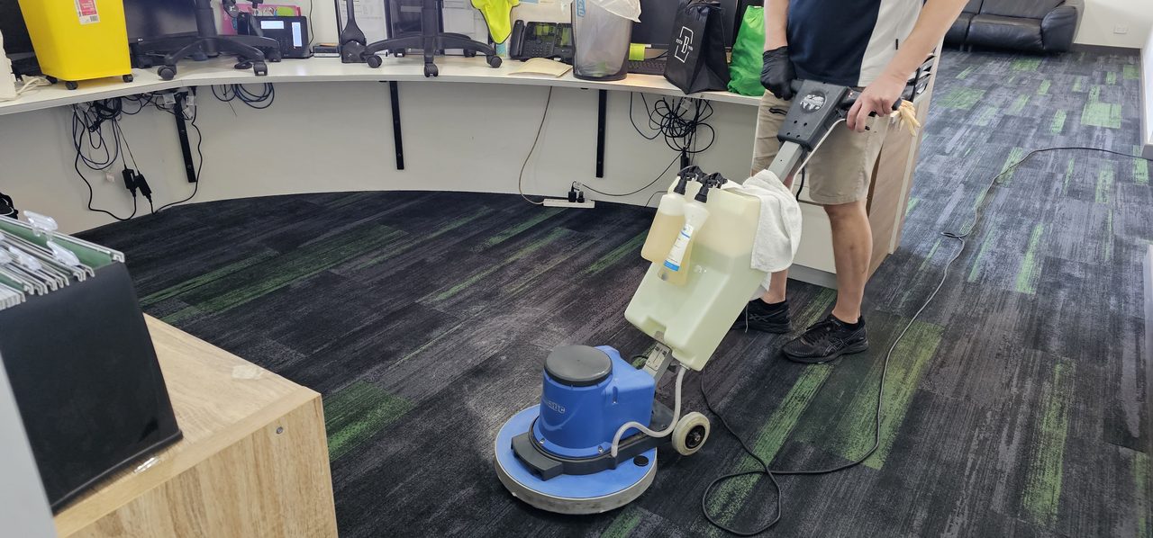 Charcoal and lime green carpet planks scrubbed around a curved Perth reception desk, the tile construction checked before any method is chosen