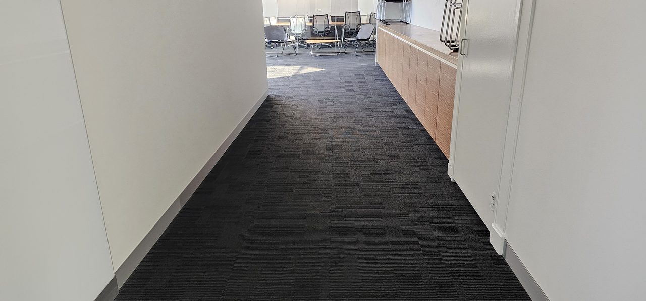 Charcoal carpet tiles along a narrow Perth corridor, the kind of shared space where a one-off spill needs a quick, authorised clean
