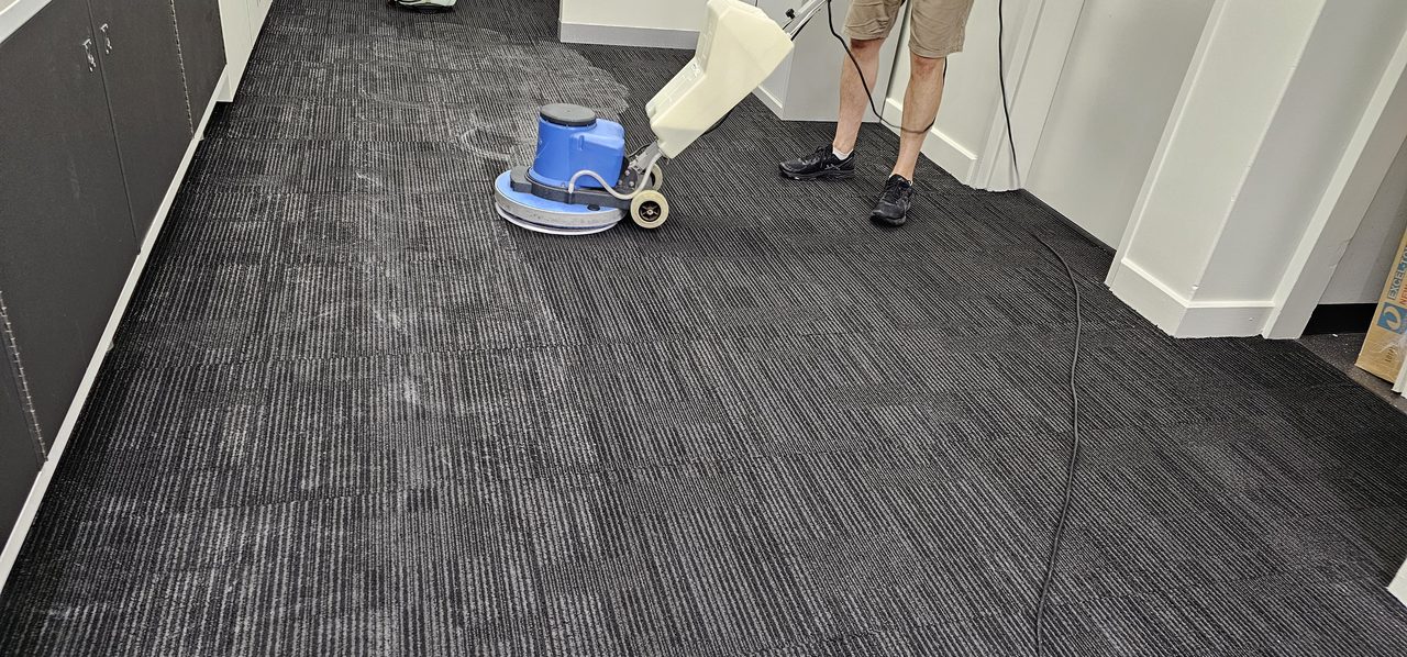 A scrubbing machine pass across charcoal carpet tiles in a Perth office bay, worked close to the partitions so the edges match the centre