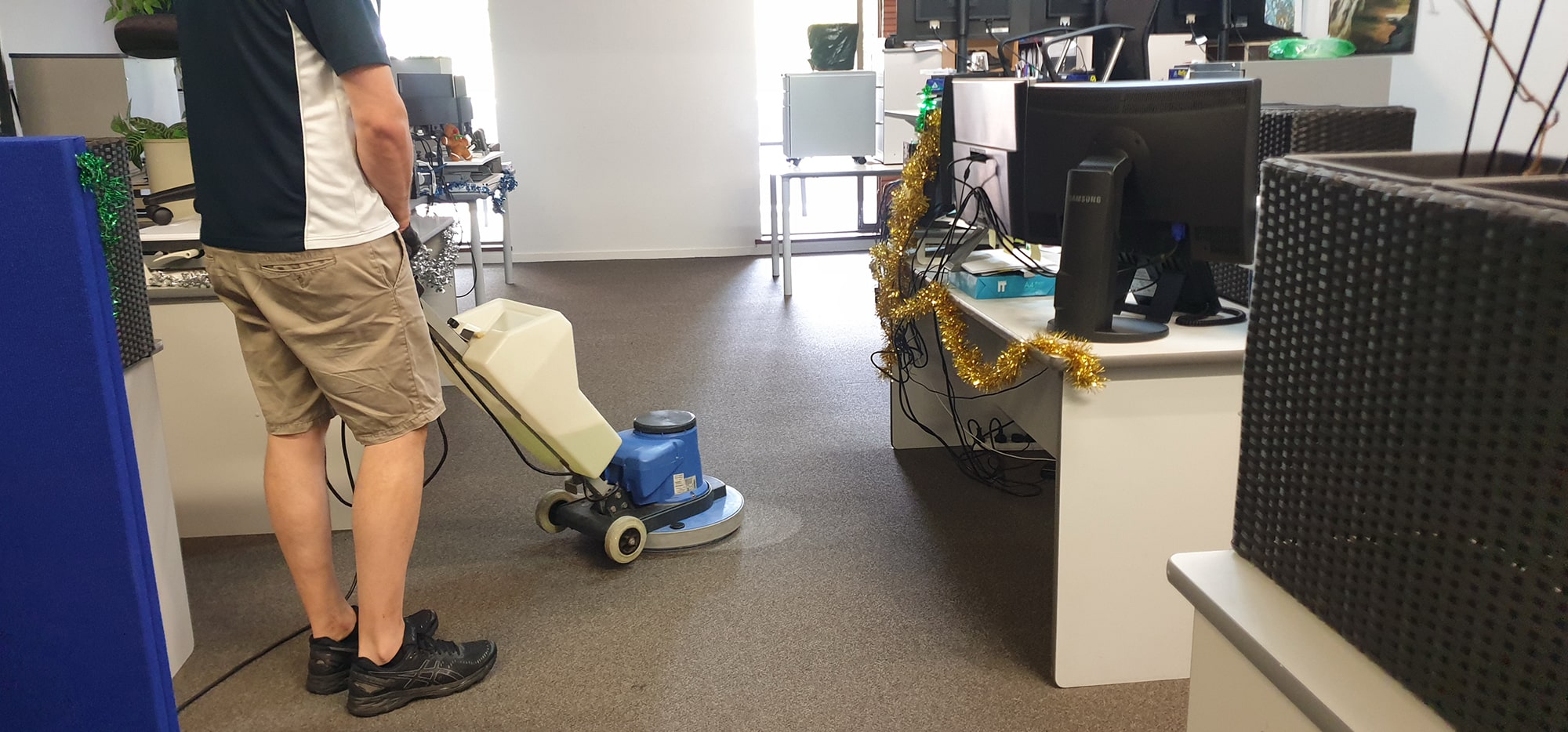 Office carpet cleaned between the occupied desks of a Perth workplace, the scrubbing machine reaching close to the furniture
