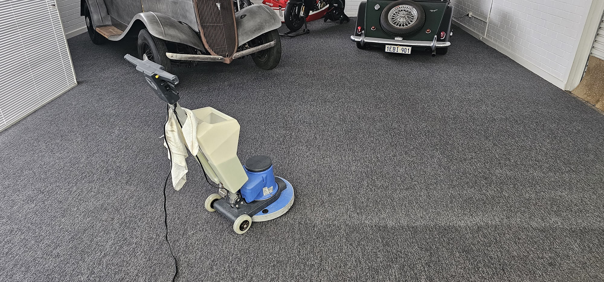 Scrubbing the charcoal carpet of a Perth classic car display, so the vehicles stand on a fresh, clean floor