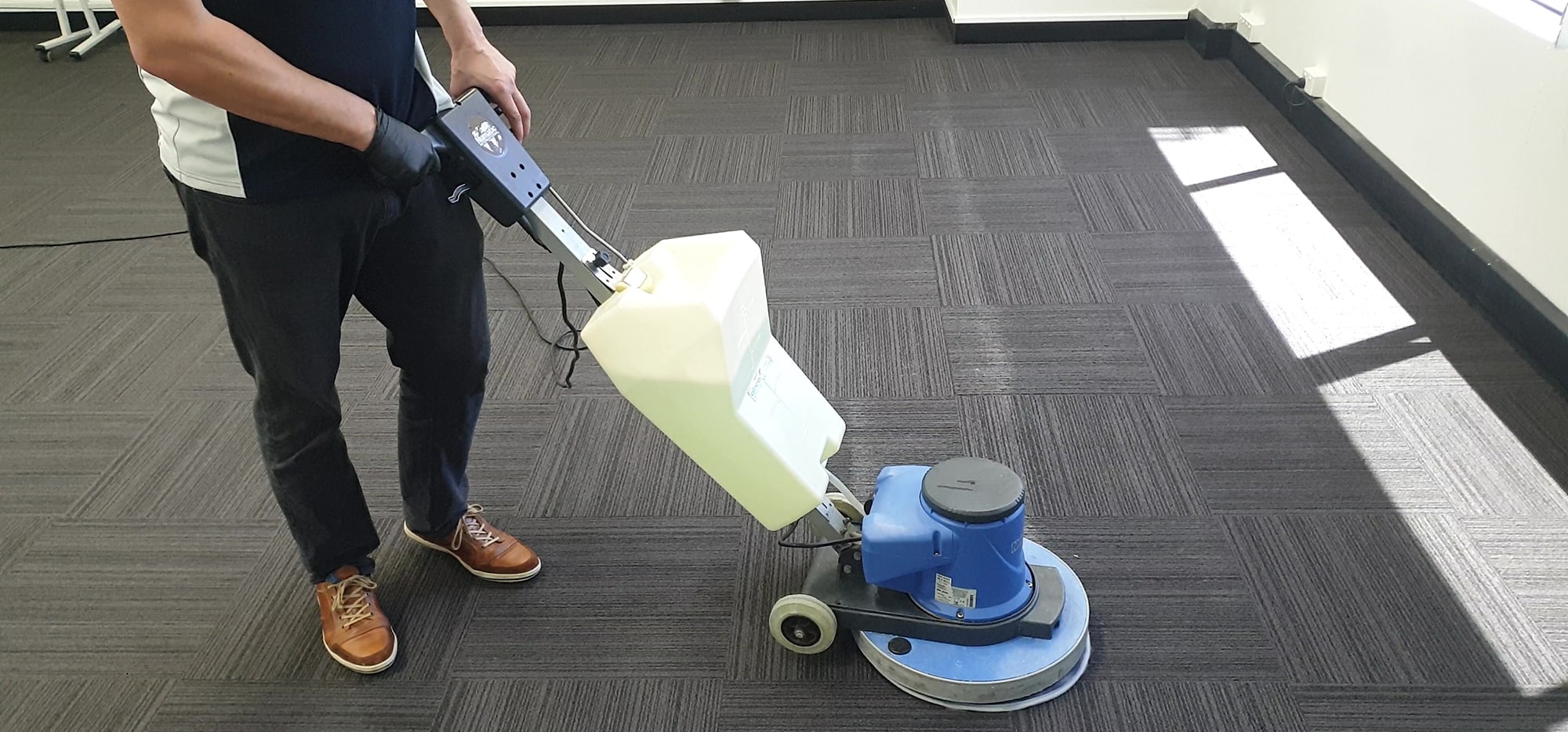Our technician working a scrubbing machine over quarter-turn carpet tiles in a sunlit Perth office