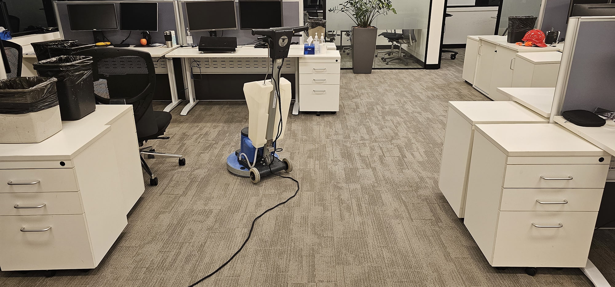 Carpet cleaned between desk pedestals in a Perth open plan office, the machine working around furniture left in place