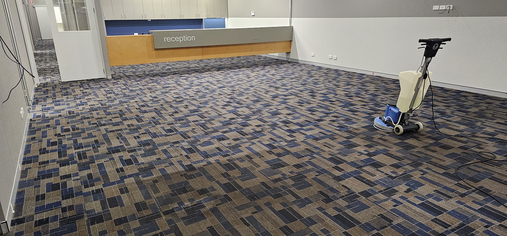 A scrubbing machine at work across the patterned carpet tiles of a Perth office reception, the first floor visitors see