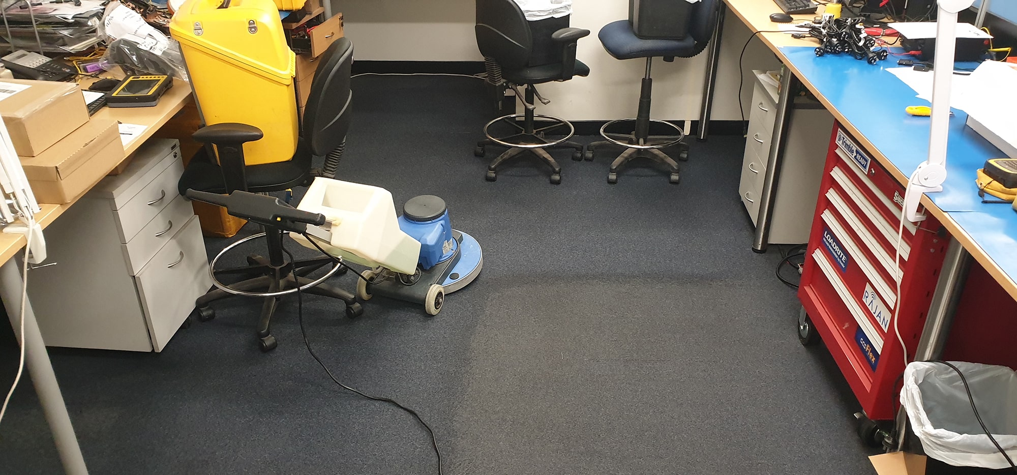 Navy carpet cleaned between the workbenches of a Perth technical workshop, the scrubbing machine fitting the tight spaces