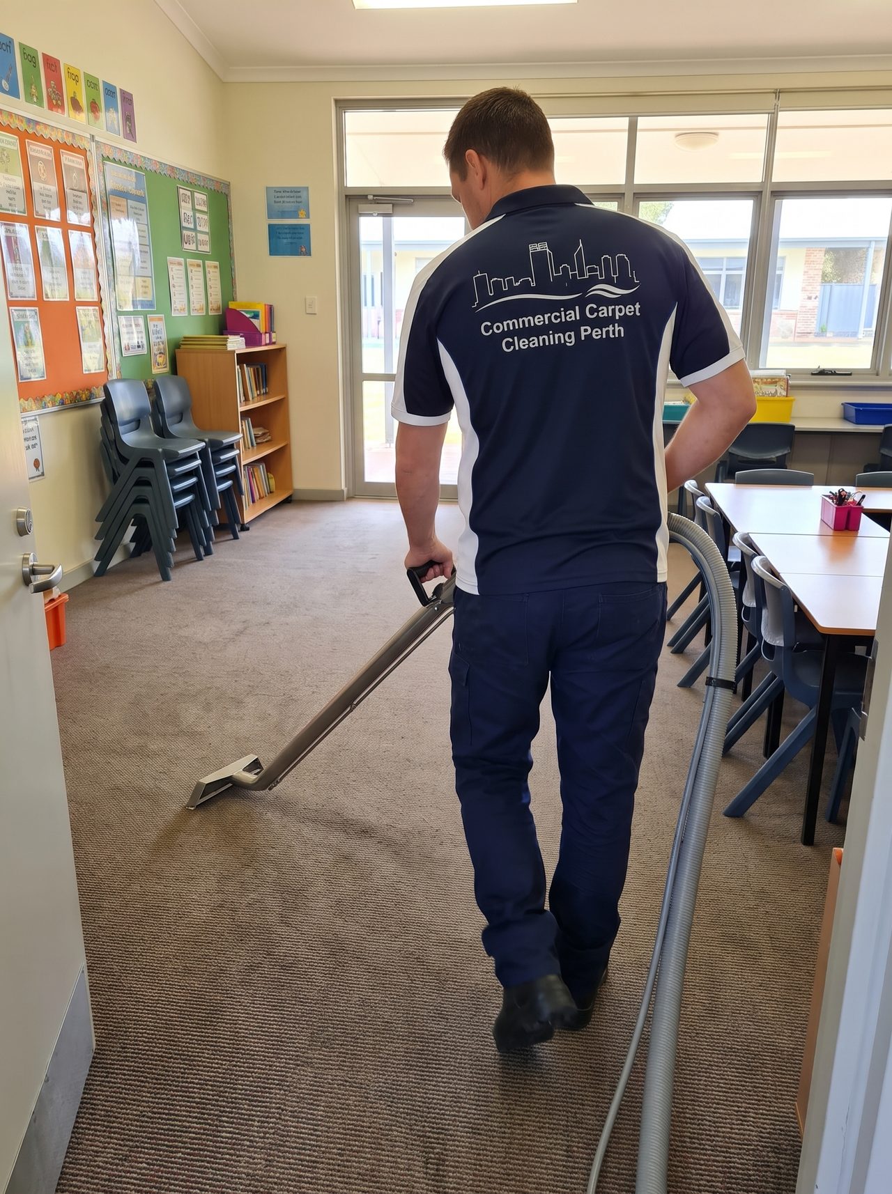 Our technician steam cleaning a school classroom carpet in Perth, the extraction wand working between the desks with the chairs stacked clear.