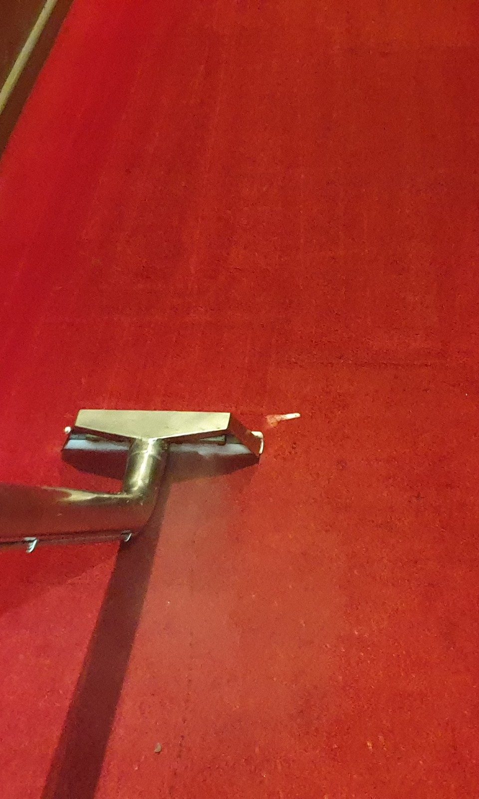The steam cleaning wand rinsing a cinema aisle in Perth, the carpet's deep red back behind each pass.