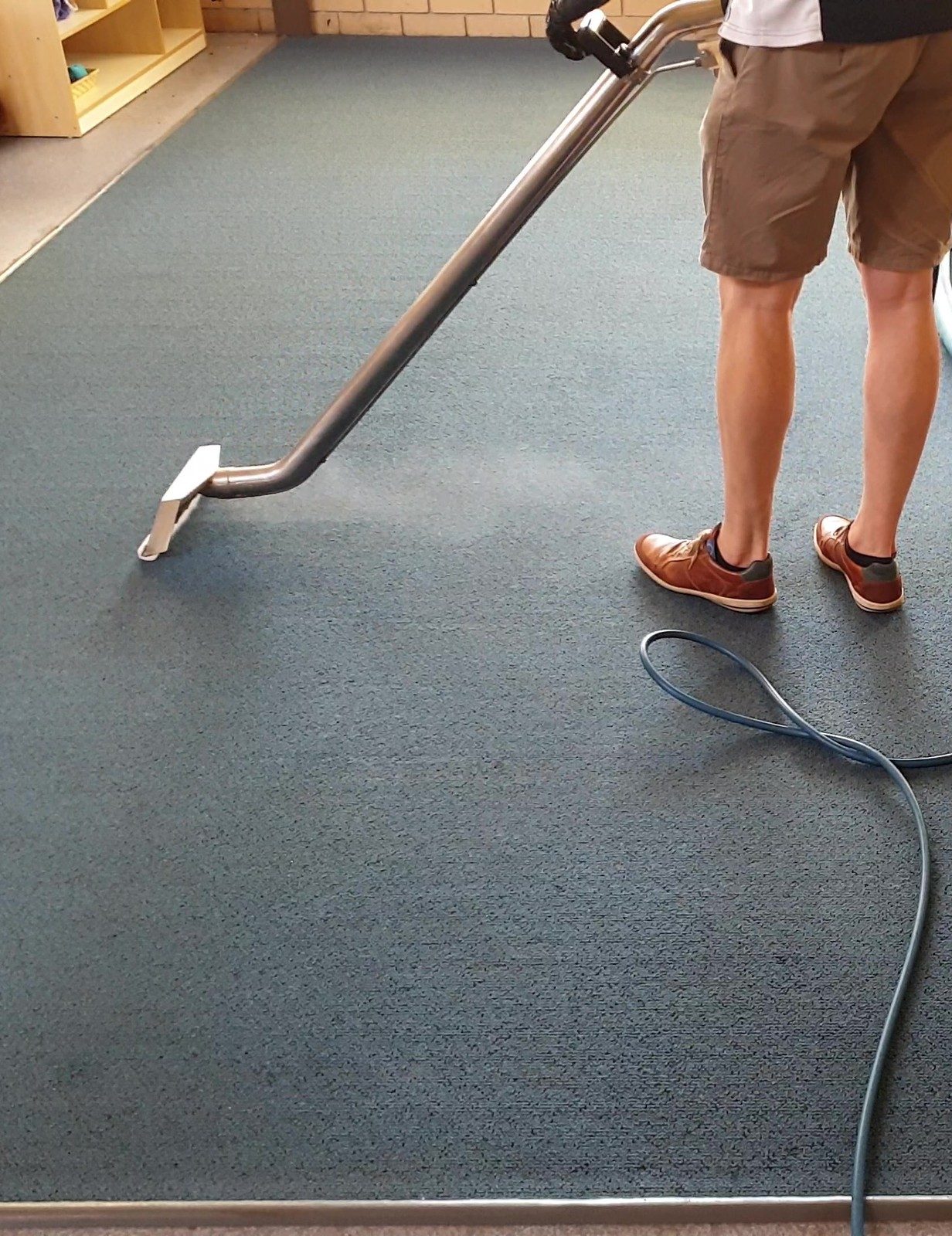 Hot water extraction in a Perth childcare room, the wand rinsing the blue carpet as the solution line trails behind.