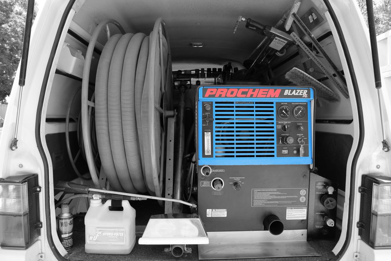 The truck-mounted carpet cleaning unit in the back of our van, with its hose reel and a floor tool beside it.