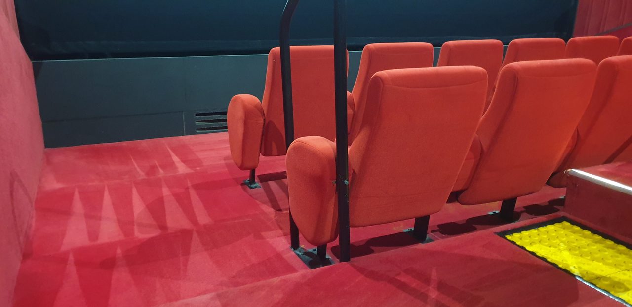 Red cinema carpet in Perth cleaned around fixed seating and the wheelchair row, fresh wand strokes right up to the seat legs.