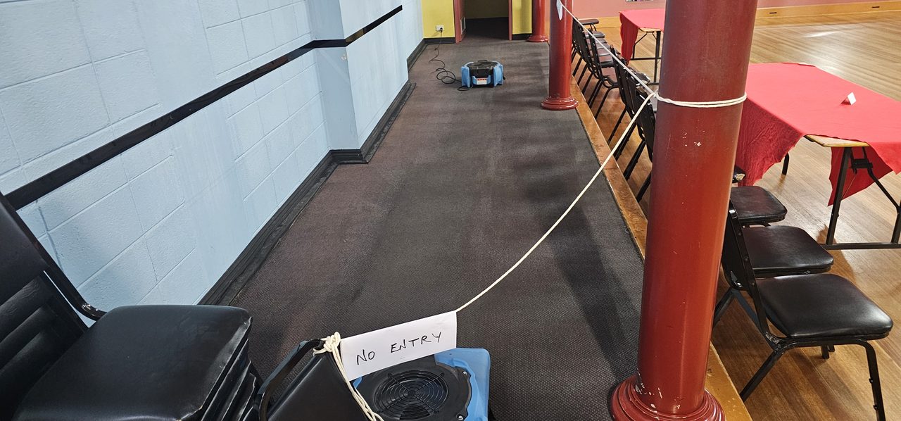 A wet stretch of carpet in a Perth function hall roped off while an air mover dries it, the rest of the room left set for use.