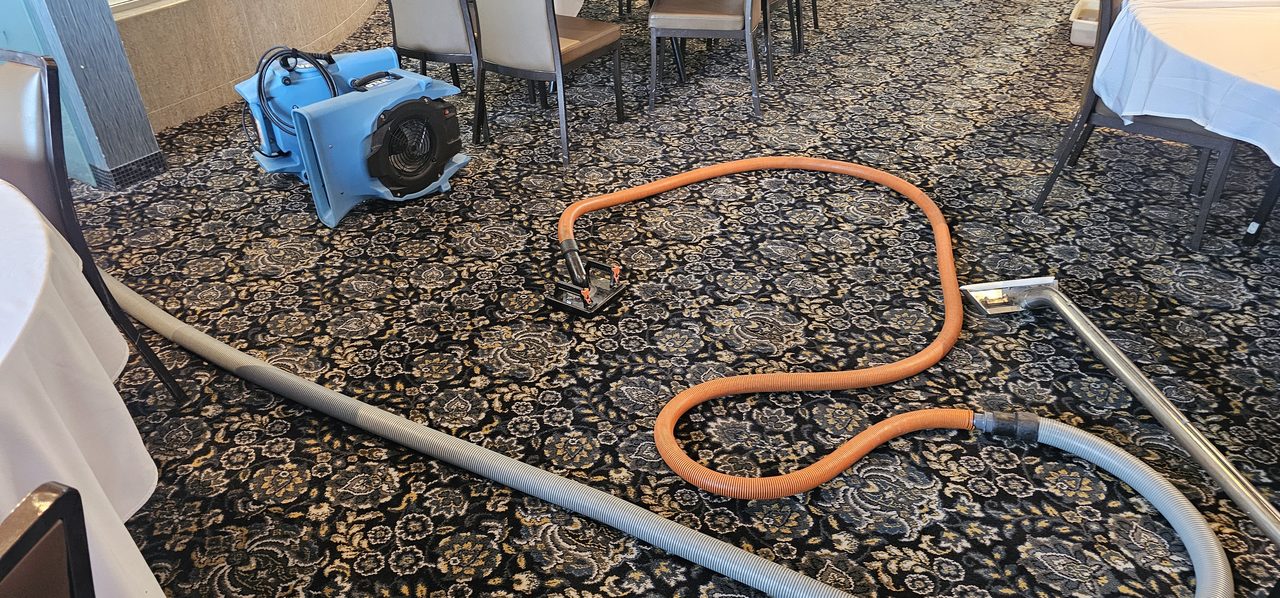 Flood extraction tools and a wand laid out on a Perth function room's carpet, with an air mover ready to start the drying.